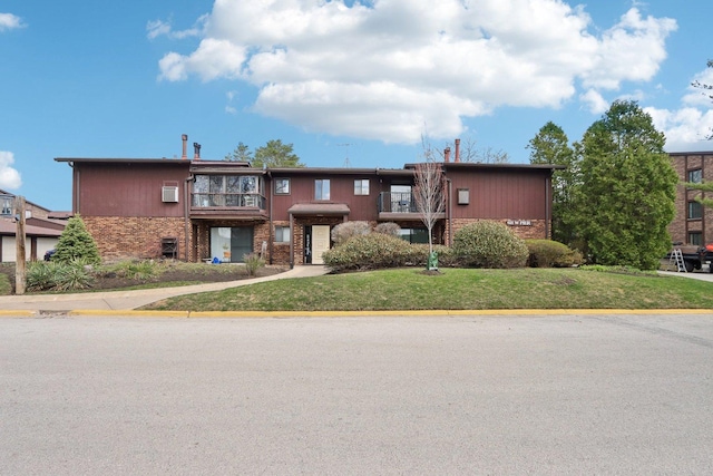 view of front facade with brick siding, a front lawn, and a balcony