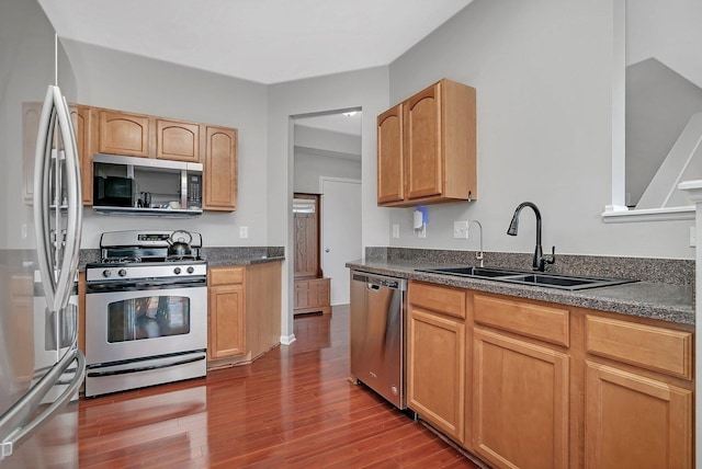 kitchen with a sink, appliances with stainless steel finishes, dark countertops, and wood finished floors