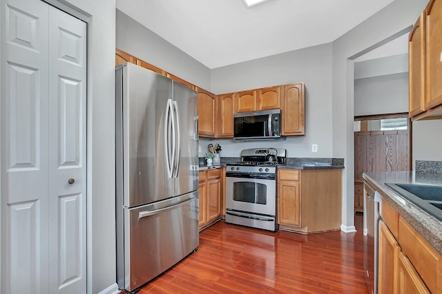 kitchen with dark wood-style flooring, stainless steel appliances, dark countertops, and baseboards