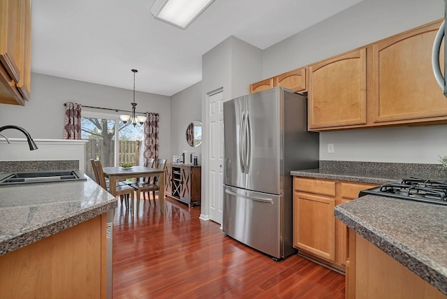 kitchen featuring an inviting chandelier, freestanding refrigerator, dark wood-style flooring, dark countertops, and a sink