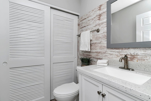 half bathroom with toilet, wood walls, and vanity