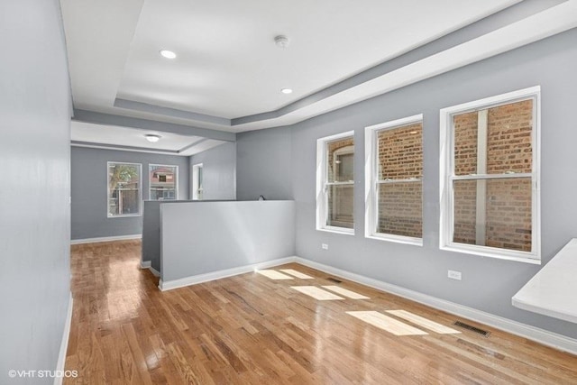 spare room with visible vents, wood finished floors, baseboards, a raised ceiling, and recessed lighting