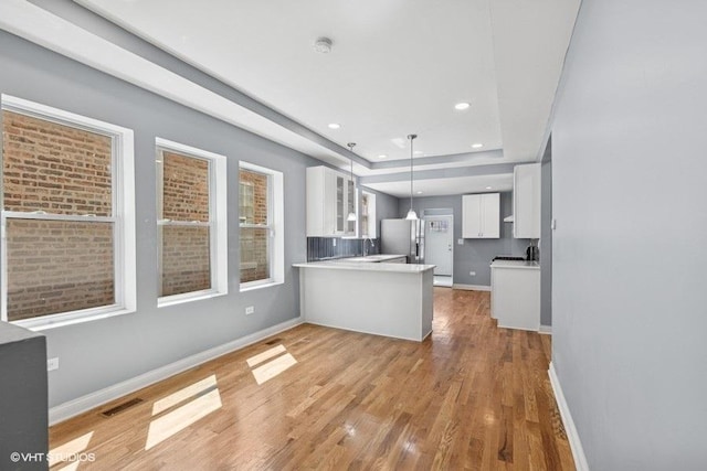 kitchen with light wood-style flooring, white cabinetry, a peninsula, visible vents, and glass insert cabinets