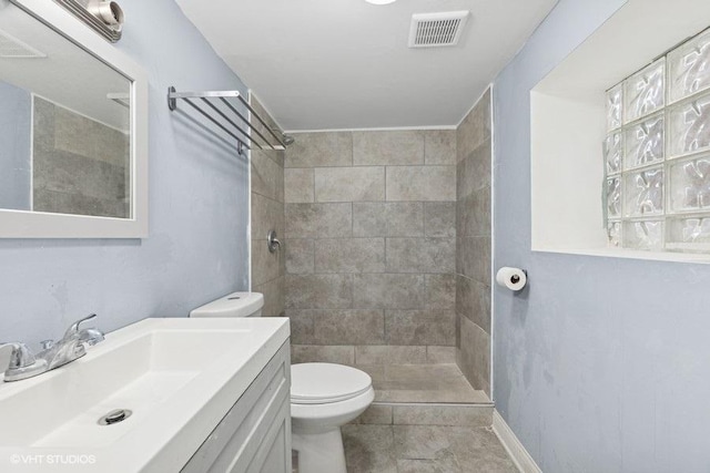 bathroom featuring toilet, visible vents, tiled shower, and vanity