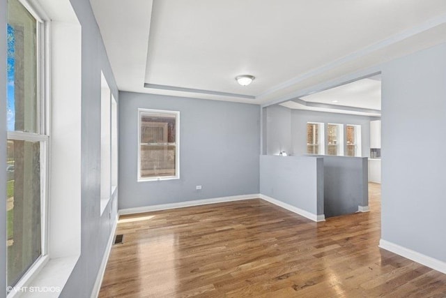 empty room with a raised ceiling, baseboards, wood finished floors, and visible vents