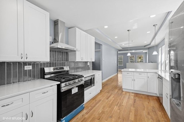 kitchen with wall chimney range hood, appliances with stainless steel finishes, tasteful backsplash, light countertops, and white cabinetry