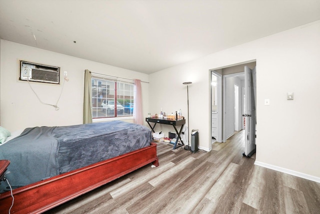 bedroom with wood finished floors, baseboards, and a wall unit AC