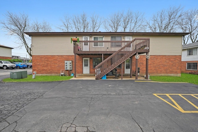 back of property with a deck, stairway, brick siding, and uncovered parking
