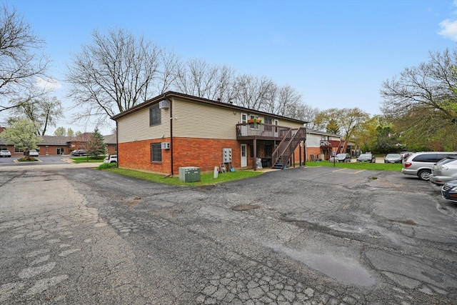 view of side of home featuring a deck, brick siding, uncovered parking, stairway, and central AC unit