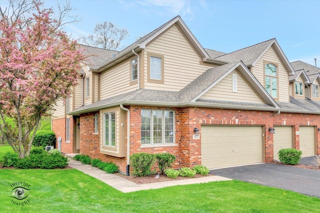 view of front facade featuring brick siding, a shingled roof, a front lawn, and aphalt driveway