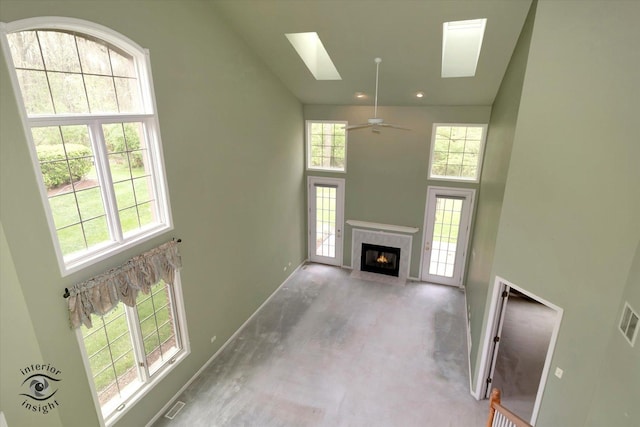 unfurnished living room with finished concrete floors, visible vents, a skylight, a fireplace, and a high ceiling
