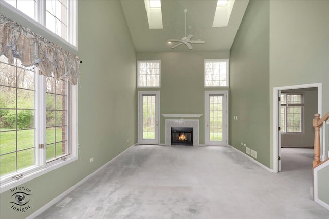 unfurnished living room featuring baseboards, high vaulted ceiling, a skylight, carpet, and a premium fireplace