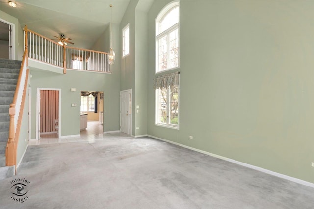 unfurnished living room featuring stairs, a towering ceiling, light carpet, baseboards, and a ceiling fan