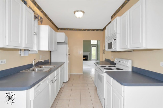 kitchen featuring dark countertops, white appliances, white cabinetry, a sink, and light tile patterned floors