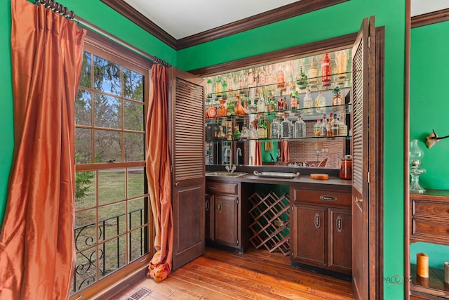 bar with ornamental molding, a sink, bar area, and light wood-style flooring