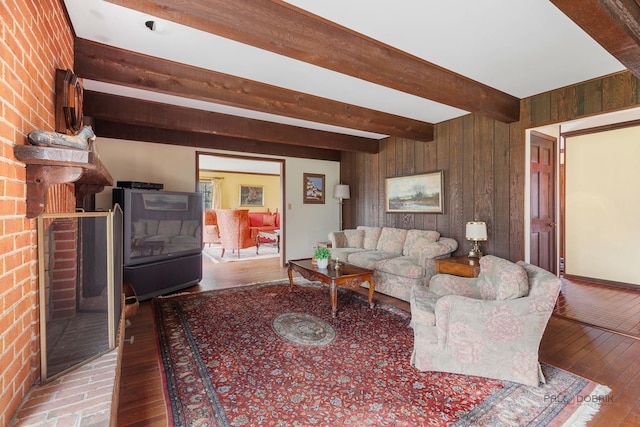 living area featuring wooden walls, a brick fireplace, beam ceiling, and hardwood / wood-style flooring