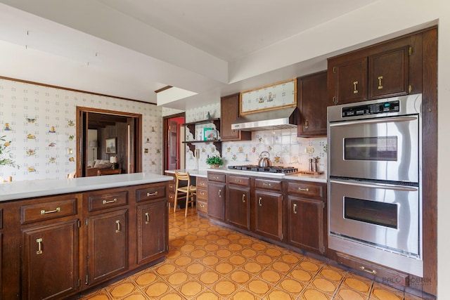 kitchen with double oven, light countertops, under cabinet range hood, and wallpapered walls