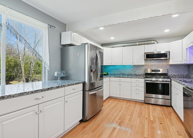 kitchen with light wood-style flooring, appliances with stainless steel finishes, backsplash, and white cabinetry