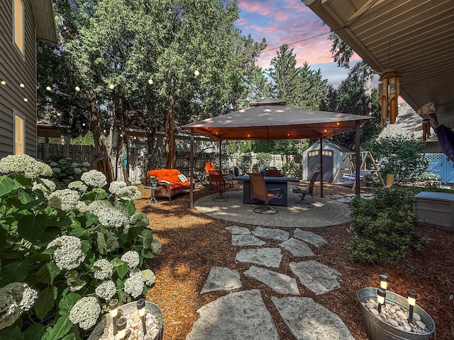 1402 W Lincoln Blvd, Freeport, IL 61032 - patio terrace at dusk featuring a gazebo, a storage unit, a fenced backyard, and a patio area