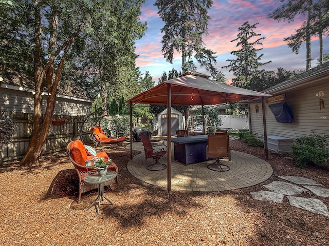 1402 W Lincoln Blvd, Freeport, IL 61032 - patio terrace at dusk with a gazebo, a storage shed, a fenced backyard, a patio area, and a grill