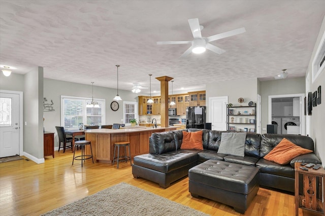 living room featuring independent washer and dryer, a ceiling fan, a textured ceiling, and light wood finished floors