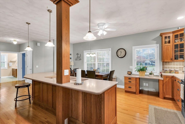 kitchen with brown cabinets, tasteful backsplash, light countertops, light wood-style flooring, and a kitchen bar