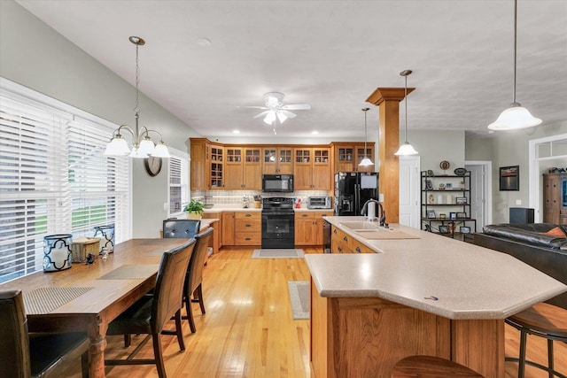 kitchen with a sink, light wood finished floors, light countertops, glass insert cabinets, and black appliances