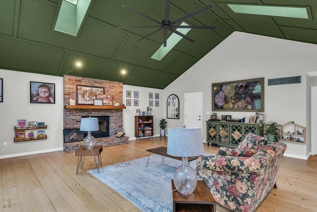living room with wood-type flooring, a fireplace, ceiling fan, high vaulted ceiling, and a skylight