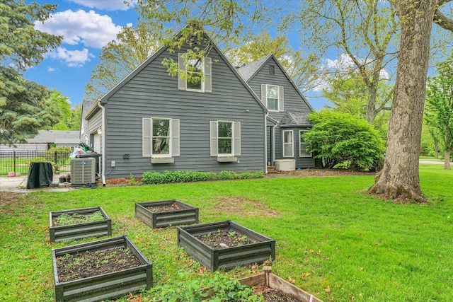rear view of house with fence, a lawn, central AC, and a vegetable garden