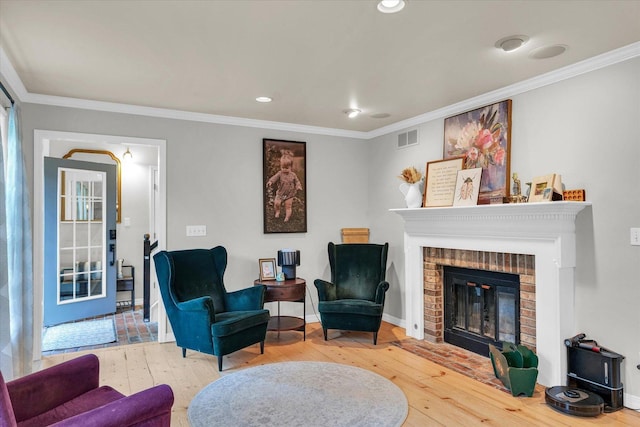living area with crown molding, a brick fireplace, hardwood / wood-style flooring, and visible vents