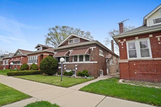 bungalow-style home featuring brick siding, a chimney, and a front yard