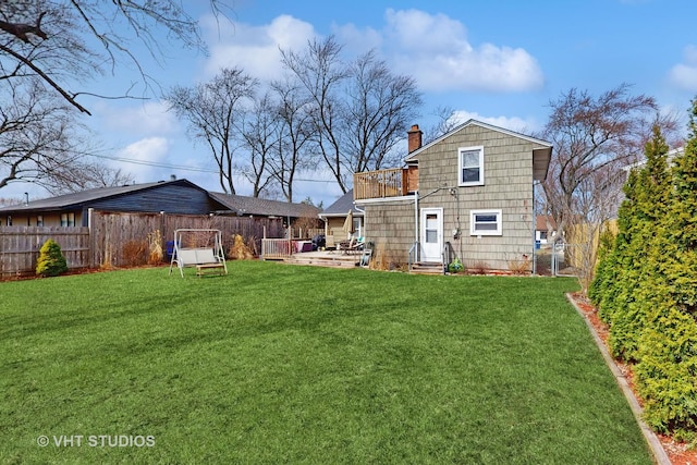 rear view of house featuring a fenced backyard, entry steps, a chimney, a balcony, and a lawn