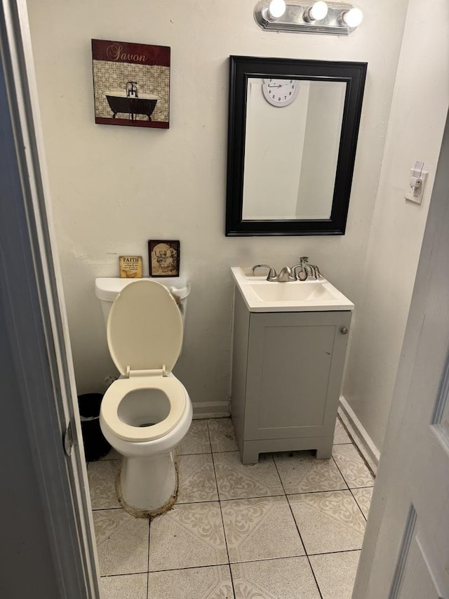 half bathroom featuring tile patterned floors, baseboards, vanity, and toilet