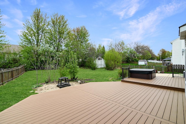 wooden terrace featuring a lawn, an outbuilding, a hot tub, a shed, and a fenced backyard