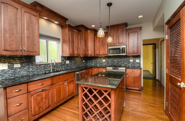 kitchen with a kitchen island, light wood-style floors, dark stone counters, a sink, and stainless steel appliances