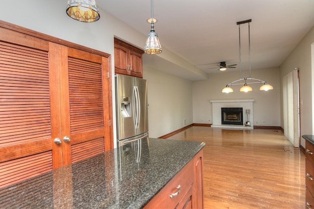 kitchen with a ceiling fan, stainless steel refrigerator with ice dispenser, hanging light fixtures, a brick fireplace, and light wood finished floors