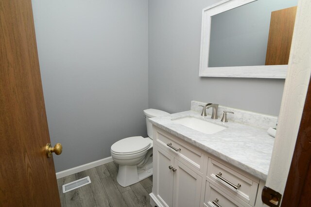 half bathroom with visible vents, vanity, wood finished floors, toilet, and baseboards