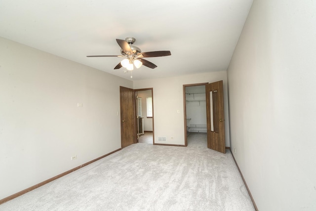 unfurnished bedroom with a closet, baseboards, a walk in closet, ceiling fan, and light colored carpet