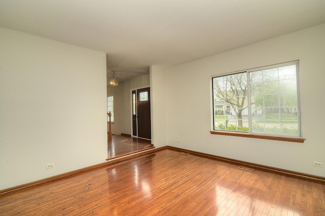 empty room featuring visible vents, wood-type flooring, and baseboards