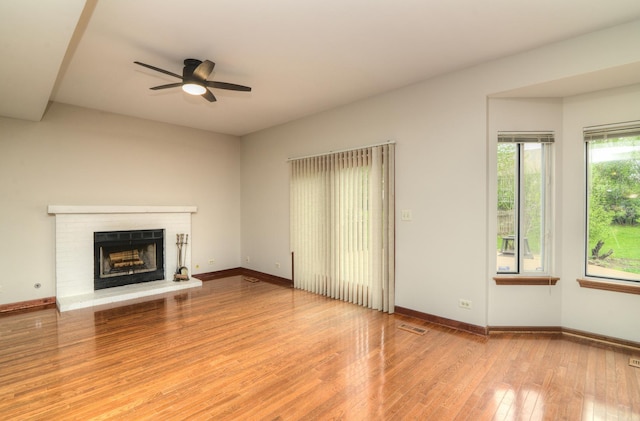 unfurnished living room featuring ceiling fan, visible vents, a fireplace, wood finished floors, and baseboards