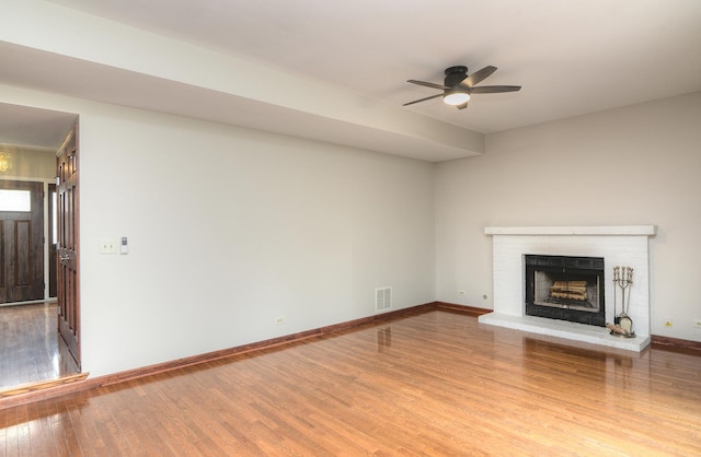 unfurnished living room featuring a ceiling fan, visible vents, a fireplace, wood finished floors, and baseboards