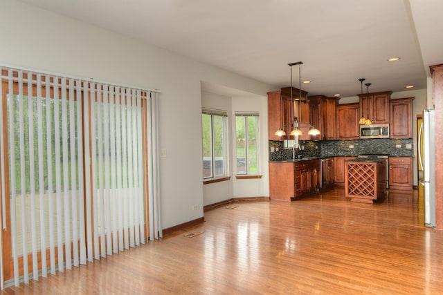 kitchen featuring brown cabinetry, decorative backsplash, dark countertops, a sink, and appliances with stainless steel finishes