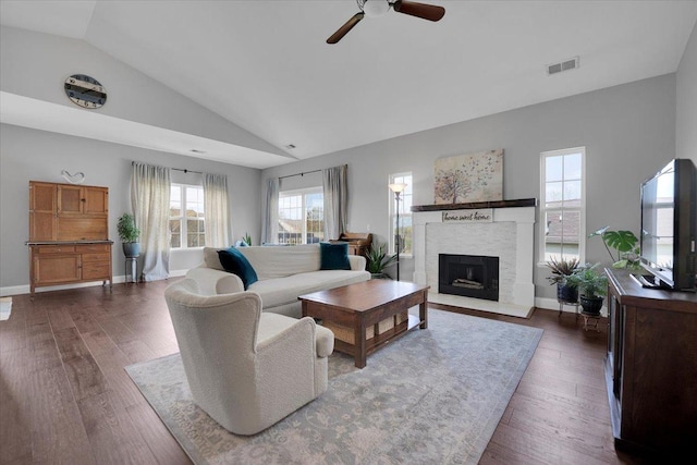 living area featuring a fireplace with raised hearth, a ceiling fan, lofted ceiling, visible vents, and dark wood-style floors
