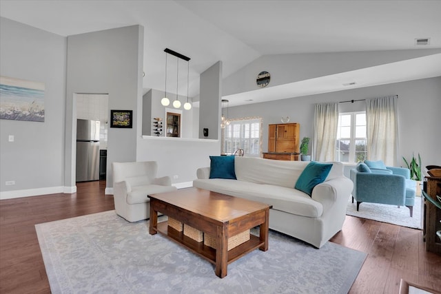 living room featuring visible vents, wood finished floors, baseboards, a chandelier, and lofted ceiling