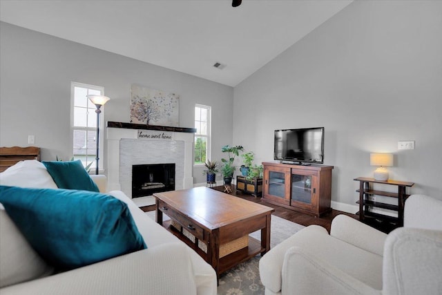 living room featuring a fireplace, high vaulted ceiling, baseboards, wood finished floors, and visible vents