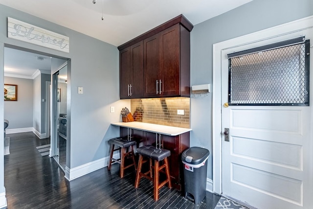kitchen with backsplash, a kitchen bar, light countertops, baseboards, and dark wood-type flooring