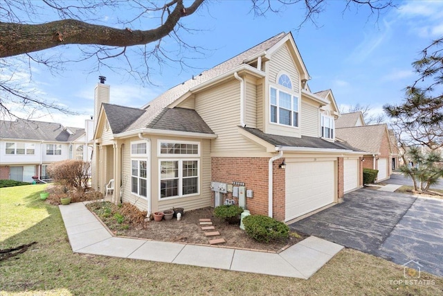 view of side of property featuring driveway, a chimney, brick siding, an attached garage, and a yard