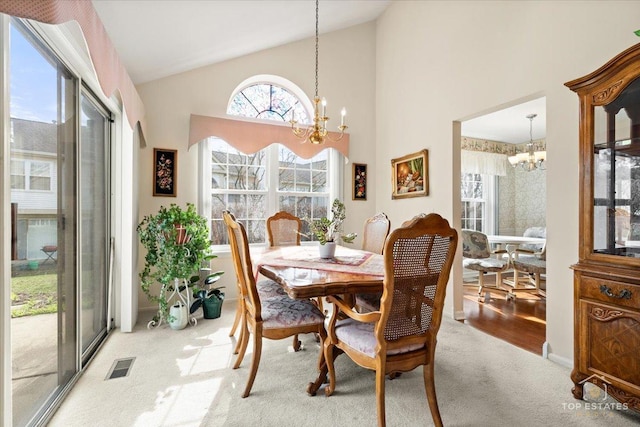 carpeted dining area with high vaulted ceiling, a notable chandelier, and visible vents