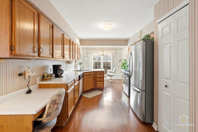 kitchen with a peninsula, wallpapered walls, light countertops, dark wood finished floors, and appliances with stainless steel finishes
