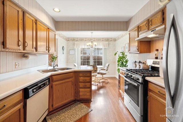 kitchen with a sink, light wood-style flooring, stainless steel appliances, wallpapered walls, and under cabinet range hood